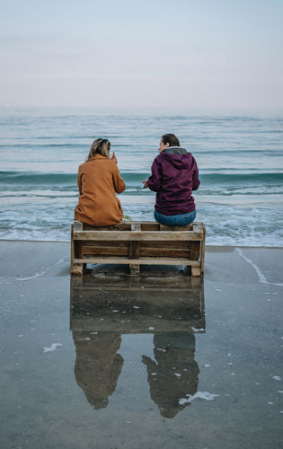 Two women sitting and talking by the body of water 